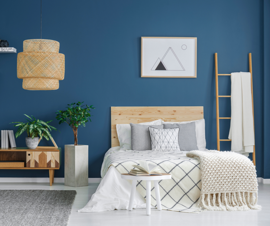 A modern bedroom utilizing 2020 themed colors to include stormy blue walls, grey planters, and a natural wood headboard.